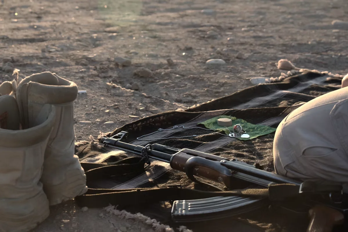 Combat boots, rifle, dog tags, and prayer stone on desert sand